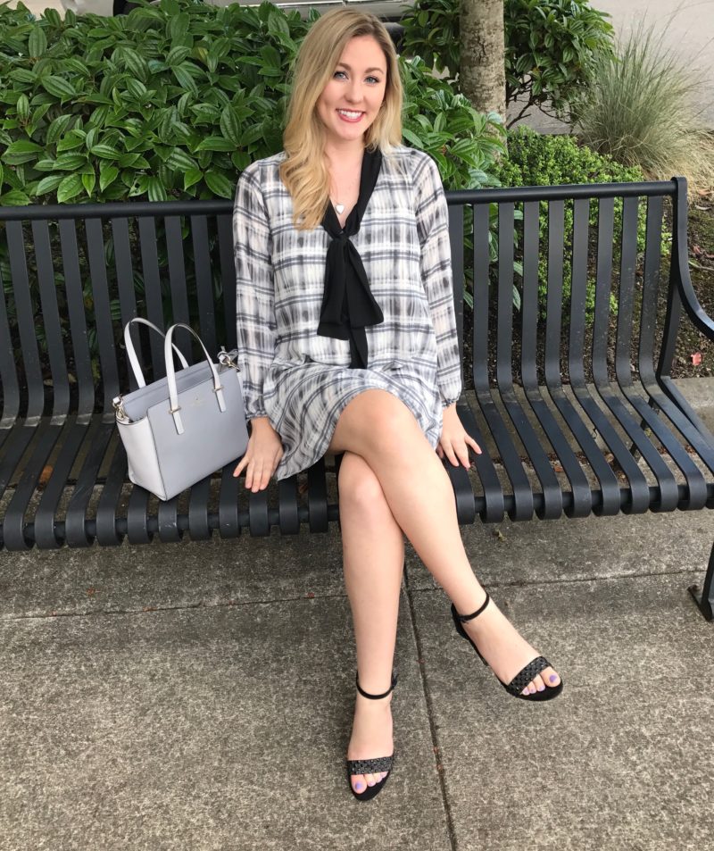 Woman in professional dress poses on a park bench with her purse